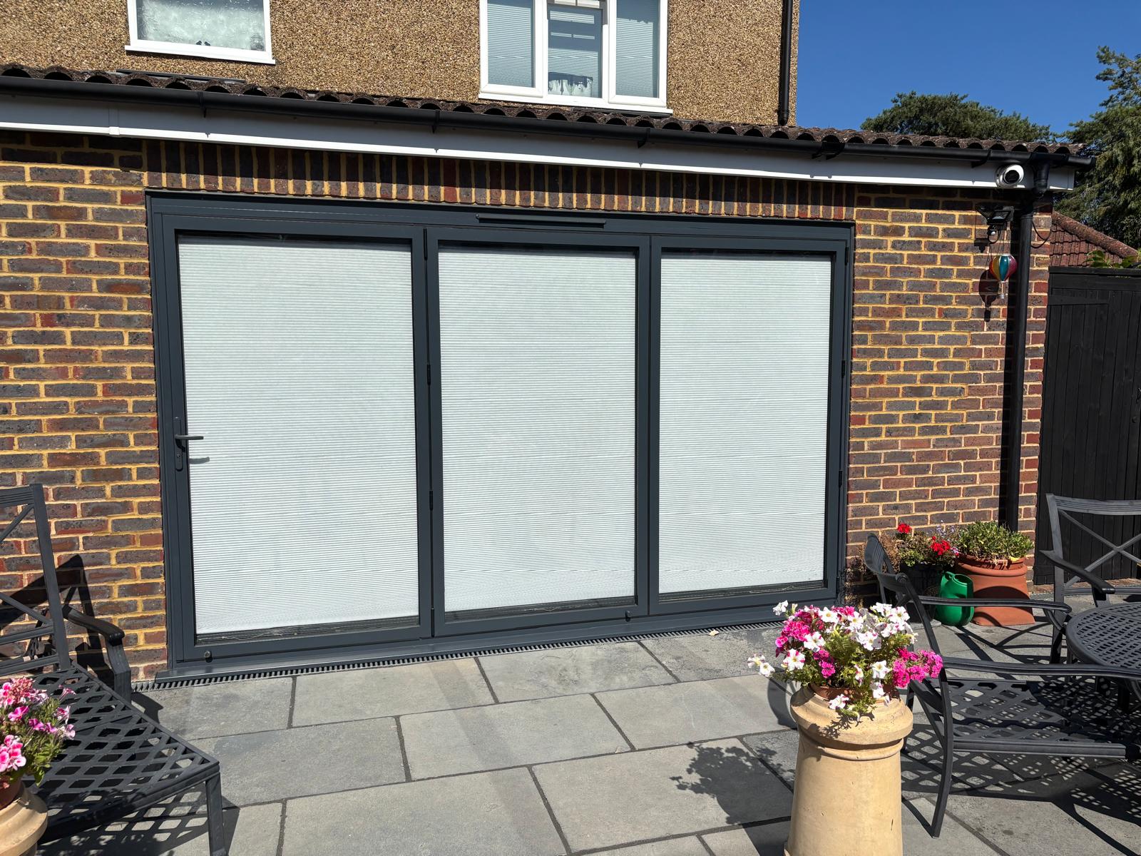 Finished three-panel grey aluminium bi-fold doors opening onto the patio