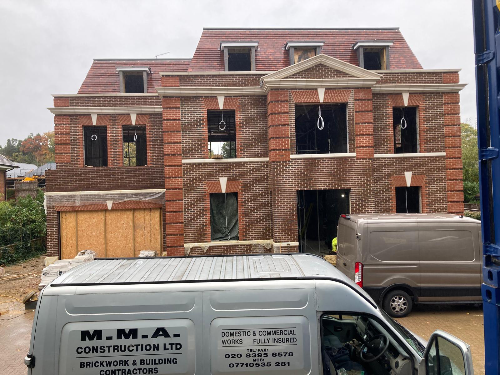 New-build house under construction with detailed brick banding and the MMA Construction van outside