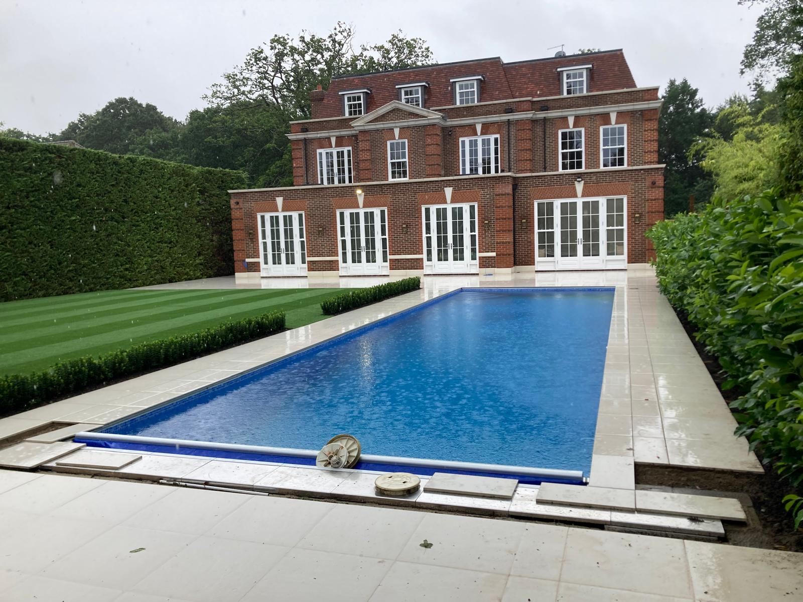 Large new-build house with completed brickwork, viewed across the finished swimming pool